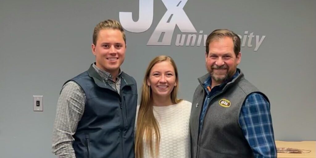 FullSizeRender Austin Freeman, Hannah Freeman, and Eric Jorgensen in front of JX Enterprises logo